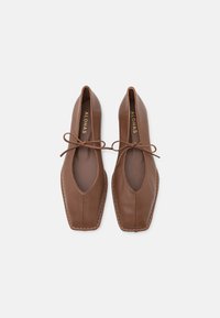 Ballerines en cuir marron avec un nez carré, des côtés ouverts et un détail en nœud à l'avant. Comprend des coutures le long de la semelle et une texture lisse.