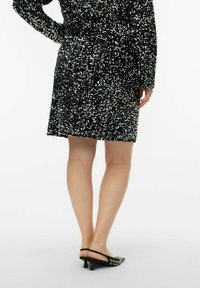 Czarna sukienka pokryta srebrnymi cekinami, z długimi rękawami, dopasowanym krojem, o długości do kolan. Noszona z czarnymi butami na obcasie z odkrytą piętą i zaostrzonym noskiem.