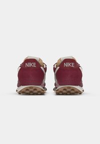 Nike tenisice u burgundiji s bijelim detaljima, s teksturiranom gornjom funkcijom, podstavljenim okovratnikom i gumeni potplat za prianjanje. Ime marke se pojavljuje na petama.