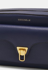 Marineblau strukturiertes Lederhandtasche mit einem goldfarbenen Verschluss und Markenlogo, mit einer glatten Oberfläche und klaren Linien. Ideal für den täglichen Gebrauch.