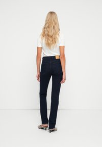 Jeans rectos de color azul oscuro con una cintura alta, tejido texturizado y un parche de cuero marrón en la parte trasera de la cinturilla.