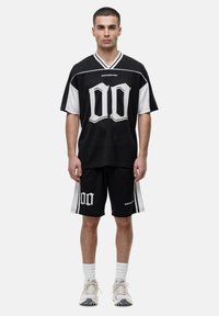 Zwart-wit oversized jersey met een mesh textuur, voorzien van gedurfde "00" graphics, gecombineerd met zwarte shorts en witte sokken.