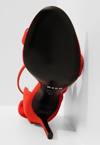 Sandale rouge à talons hauts avec bride de cheville vue du dessous, semelle noire avec inscription MSGM blanche et taille 37 imprimée.