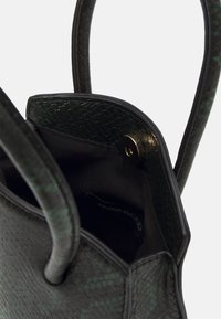 Vihreä teksturoidulla käärmeen nahkakuviolla varustettu käsilaukku. Siinä on pitkät mustat kahvat ja sisällä magneettinen napsautussuljin. Sisäosa on kangaspäällysteinen.