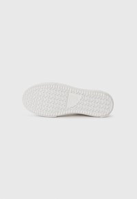 White rubber shoe sole with a zigzag tread pattern, featuring a smooth texture and a triangular logo embossed in the center.