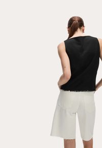 Zwarte mouwloze top met een rafelige zoom, gecombineerd met lichtbeige hoge taille shorts met achterzakken en een rechte snit.