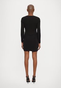Čierne bodycon šaty s dlhými rukávmi, okrúhlym výstrihom a zipsom na chrbte. Prezentujú priliehavý strih a dĺžku po kolená. Čierne ihlové topánky.