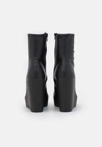 Melnas potītes zābaki, izgatavoti no gludas ādas, ar pieguļošu dizainu, augstiem kvadrātveida papēžiem un aizmugurējo rāvējslēdzēju aizdarei.