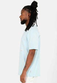 Ljusblå bomullströja med avslappnad passform, korta ärmar och kontrasterande broderade detaljer. Har en sidetikett nära fållen.