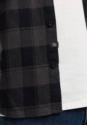 Svart- och grårutigt flanellskjorta med knäppning och logotagg, lager över en vit T-shirt. Texturerat tyg med mjuk yta.