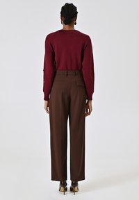 Maglione lavorato a maglia bordeaux con maniche lunghe, abbinato a pantaloni marroni a vita alta e a gamba larga. Scarpe nere con tacco e un finish lucido.