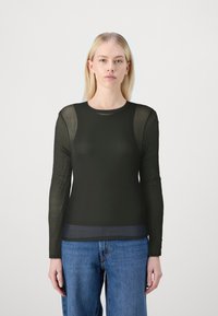 Svart långärmad topp med genomskinligt tyg på ärmarna, rundad halsringning och figursydd kropp. I kombination med blå jeans, minimalistisk design.