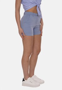 Pantaloni corti azzurro chiaro in misto cotone, con tasche frontali e cuciture decorative, abbinati a sneakers bianche.
