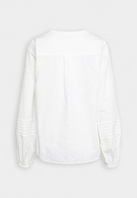 Blusa bianca con un motivo a pois testurizzati, maniche lunghe a sbuffo con dettagli plissettati e scollatura rotonda. Vista posteriore.