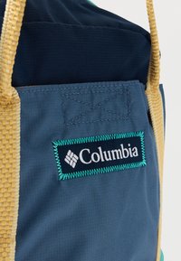 Μπλε υφασμάτινη τσάντα με πλεκτές λαβές σε χρώμα καφέ. Διαθέτει ραμμένο λογότυπο σε λευκό και τυρκουάζ με διαμάντι μοτίβο.