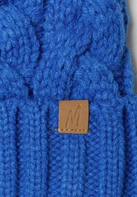 Bonnet tricoté bleu en laine épaisse avec un motif tressé. Comprend une petite étiquette en cuir brun avec un "M" embossé.