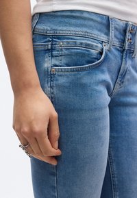 Τζιν παντελόνι από μπλε ντένιμ με εφαρμοστή γραμμή και διακριτική ξεθωριάδα, σχεδιασμό με πέντε τσέπες και εμφανείς ραφές κατά μήκος των ενώσεων.