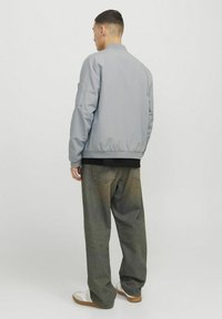 Graue Bomberjacke mit geripptem Kragen, elastischen Bündchen und Saum. Kombiniert mit dunklen, locker sitzenden Jeans und weißen Sneakers. Schlichtes Design.