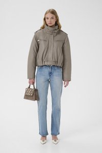 Szürke bőr rövidített dzseki magas gallérral és ezüst cipzárakkal, világoskék egyenes szárú farmerrel, fehér hegyes orrú cipővel és barna pöttyös táskával párosítva.