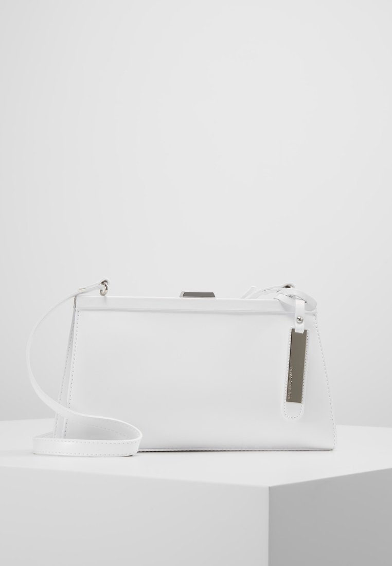 Biała skórzana torebka o strukturalnym designie, z długim, odczepianym paskiem oraz srebrną metką. Posiada gładką fakturę i minimalne detale.