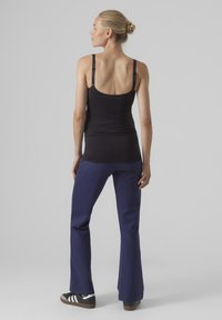 Zwarte tanktop met dunne banden, gecombineerd met marineblauwe flarebroek en donkere sneakers met witte accenten; zachte stof met een aansluitend ontwerp.