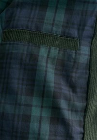 Geruite stof in donkergroen en marineblauw, met een geribbelde donkergroene accentkleur. Bevat een horizontale zak met een gestructureerde afwerking.