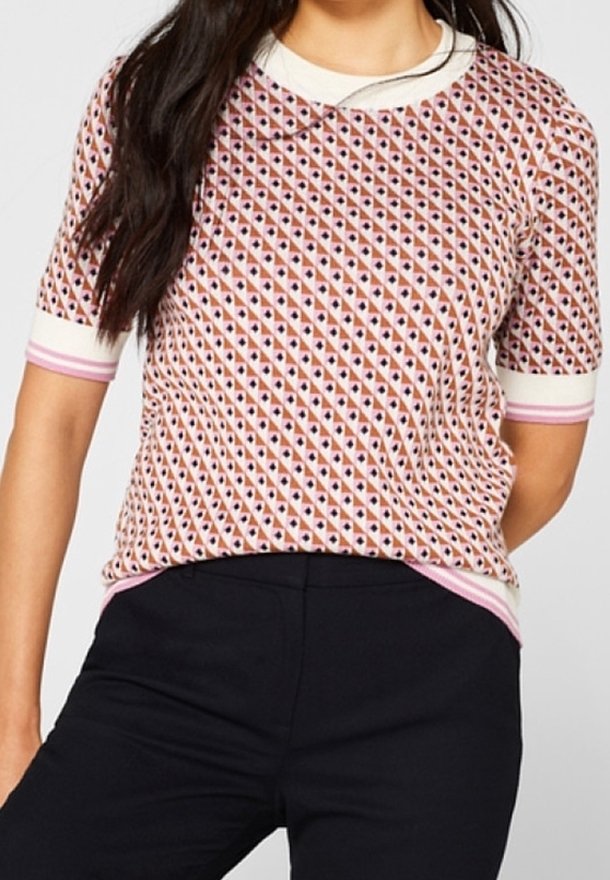 Mujer con una blusa de manga corta con un diseño geométrico en rosa, blanco y negro, combinada con pantalones negros.