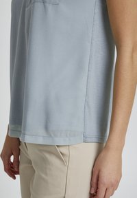 Lyseblå kortærmet bluse med blød tekstur og lige kant, med en subtil glans og side slids detaljer. Bæres med beige bukser.
