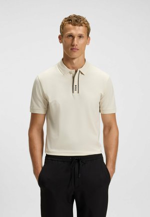 Lichtbeige polo shirt met een omgevouwen kraag, voorzien van een zwart-wit gestreepte knopenlijst. Korte mouwen en een gladde, textuurrijke stof.