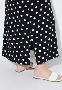 Zwarte rok met stippen, voorzien van een zijsplit, gemaakt van een gladde stof. Gecombineerd met witte instapsandalen met een gerimpeld detail.