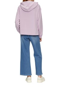 Felpa lilla con una vestibilità comoda e cappuccio, abbinata a jeans a vita alta azzurri e larghi. Sneakers bianche con suola piatta completano il look.