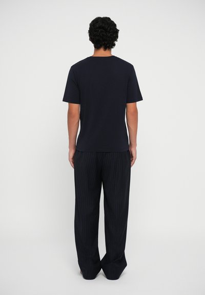 T-shirt blu navy a maniche corte con scollatura rotonda, abbinato a pantaloni a gamba larga a strisce scure, design minimalista, texture liscia.