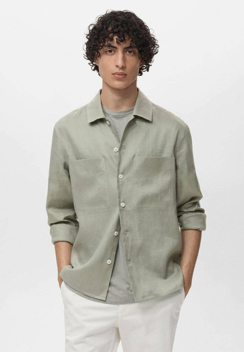 Svijetlozelena košulja sa dugim rukavima, dugmadi, dva prednja džepa i ležernim krojem, preko sive majice, uparena s bijelim hlačama.