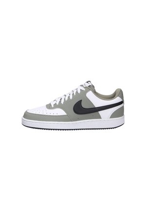 Zapatilla deportiva de corte bajo con paneles de cuero blancos y grises, logo Nike swoosh en negro, cordones blancos y suela de goma blanca con dibujo en negro.