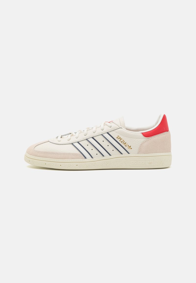 Weißer Sneaker aus Leder und rosa Wildleder mit drei dunkelblauen Streifen, rotem Fersenlasche, goldener Markenprägung und strukturierter Gummisohle. Klassisches Design.