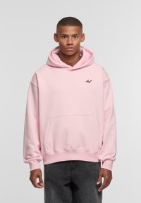 Light pink hooded sweatshirt with a front pocket and black logo on the left chest. Features a loose fit and ribbed cuffs.