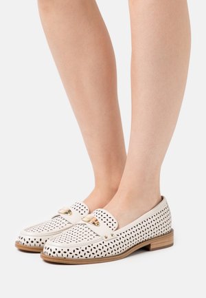 Mocassins blancs perforés avec un petit talon en bois et des accents en métal doré. Présente un dessus lisse et des motifs découpés décoratifs.