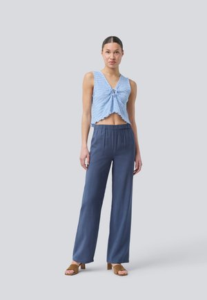 Light blue cropped top with a twisted detail at the center, paired with loose-fitting navy blue pants and brown heeled sandals.