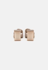Beige blokkheels mules med et teksturert stoffoverdel og transparente firkantede hæler, med åpne bak og polstrede ankelstropper.
