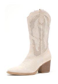 Botas de vaquero de ante beige con un intrincado diseño perforado, punta afilada y tacón apilado. Presentan costuras decorativas a lo largo del eje.