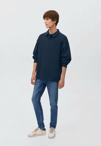 Temno modra majica s long sleeves in ovratnikom, kombinirana s svetlo modrimi kavbojkami in bež supergami, z ohlapnim krojem in mehko teksturo.