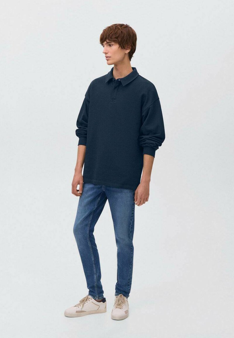 Temno modra majica s long sleeves in ovratnikom, kombinirana s svetlo modrimi kavbojkami in bež supergami, z ohlapnim krojem in mehko teksturo.