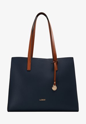 Sac cabas en cuir bleu marine avec poignées en cuir marron, logo de la marque doré et un pendentif rond en or suspendu à une poignée.