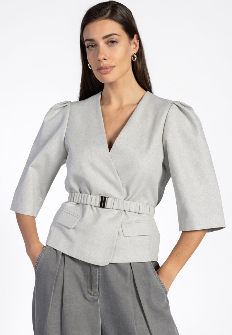 Grijze, gestructureerde wikkeltop met korte pofmouwen, een riem in de taille en twee voorzakken, gemaakt van een gladde, gestructureerde stof.