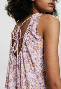 Ljuslila ärmlös topp med blommönster, har ett knyt i ryggen, rynkad struktur och öppen ryggdesign.