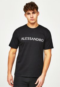 Musta puuvillapaita, jossa on sana "ALESSANDRO" valkoisella tekstillä rinnassa. Lyhyet hihat ja pyöreä kaula-aukko. Sileä pinta.