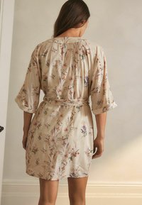 Cvjetni kimono-plašt u bež satenu s 3/4 rukavima, s pojasom na vezanje, koji ima delikatan uzorak šarenih divljih cvjetova.