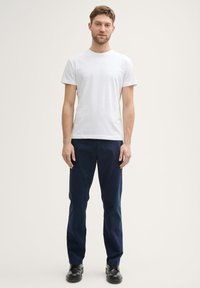 T-shirt en coton blanc et pantalon en coton bleu marine, avec une coupe droite. Des chaussures en cuir noires complètent la tenue. Design simple et classique.