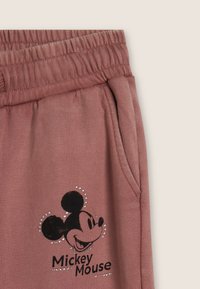 Pantalones deportivos color rosa polvo con cintura elástica, bolsillos laterales y un gráfico impreso de Mickey Mouse en negro con detalles de pedrería.