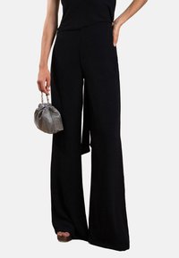 Pantalons larges noirs taille haute en tissu doux. Associés à un petit sac argenté à cordon, mettant en avant un design minimaliste.